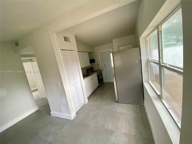 kitchen with range with electric stovetop, freestanding refrigerator, white cabinetry, baseboards, and vaulted ceiling