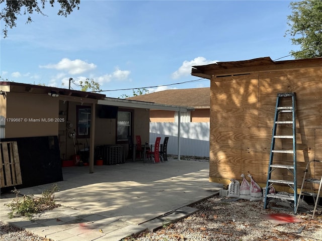 view of side of property featuring a patio, fence, roof with shingles, and stucco siding