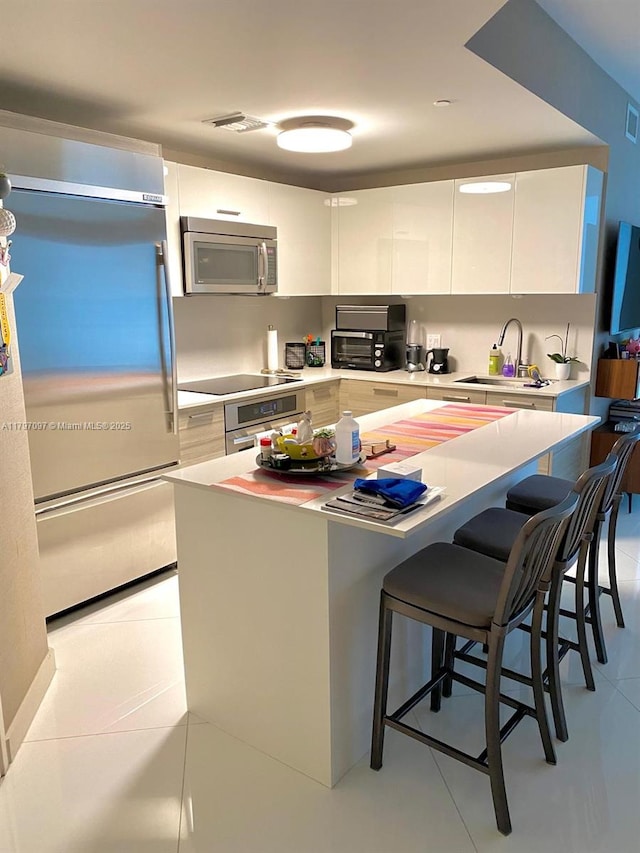 kitchen with appliances with stainless steel finishes, a sink, modern cabinets, white cabinets, and a kitchen bar