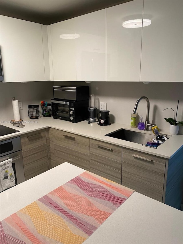 kitchen featuring modern cabinets, stainless steel oven, a sink, and light countertops