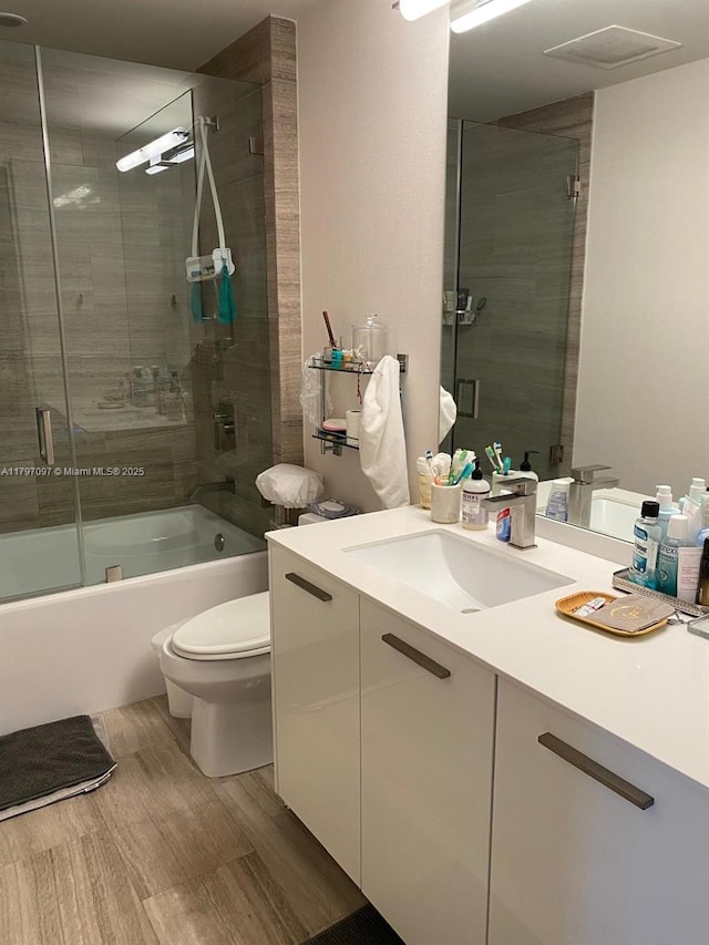 bathroom featuring toilet, shower / bath combination with glass door, and vanity