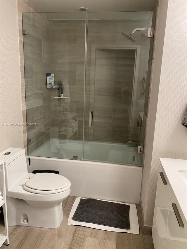 bathroom featuring enclosed tub / shower combo, toilet, wood finished floors, and vanity