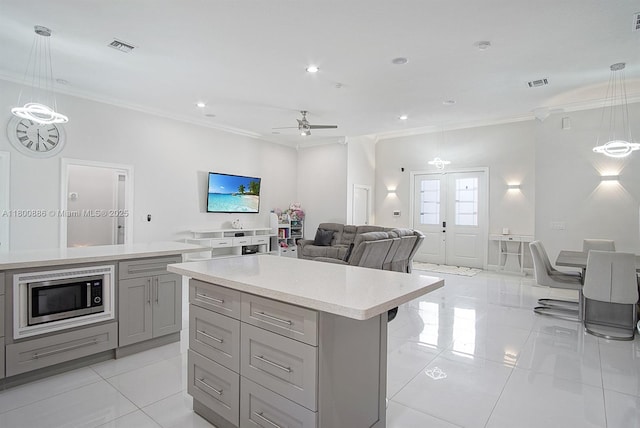 kitchen with gray cabinetry, stainless steel microwave, ornamental molding, light tile patterned floors, and light countertops