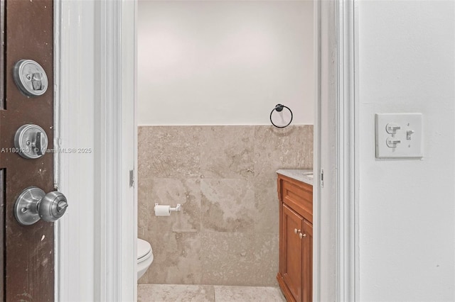 bathroom with vanity, toilet, and tile walls