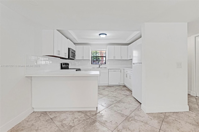 kitchen featuring appliances with stainless steel finishes, a tray ceiling, light countertops, and decorative backsplash
