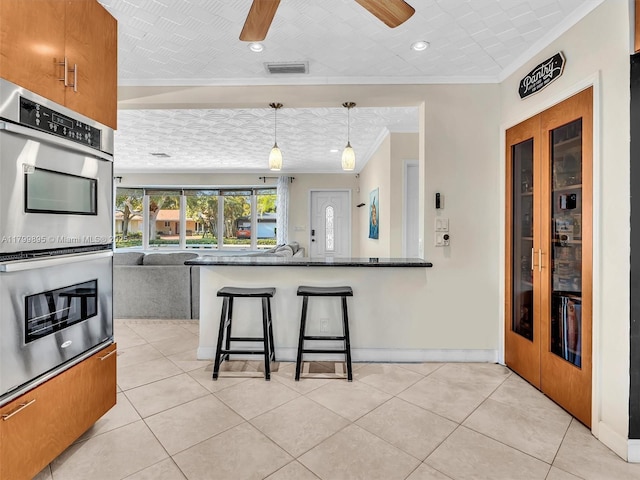 5119 Hayes St, Hollywood, FL 33021 - kitchen with stainless steel double oven, ornamental molding, a kitchen breakfast bar, a ceiling fan, and light tile patterned floors