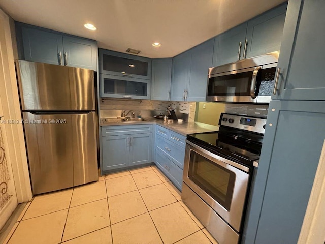 kitchen featuring appliances with stainless steel finishes, light tile patterned floors, tasteful backsplash, a sink, and glass insert cabinets