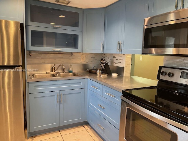 kitchen featuring appliances with stainless steel finishes, a sink, light tile patterned floors, decorative backsplash, and glass insert cabinets
