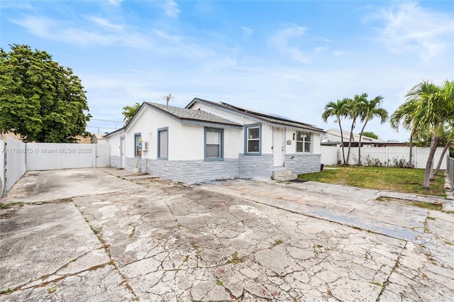 621 E 8th St, Hialeah, FL 33010 - view of front facade with stone siding, a fenced backyard, solar panels, stucco siding, and a patio