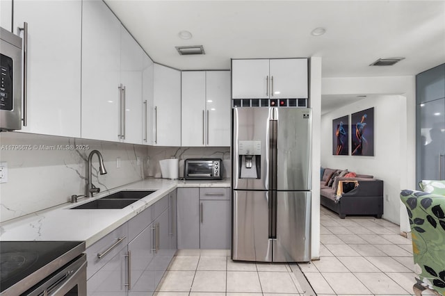 621 E 8th St, Hialeah, FL 33010 - kitchen featuring stainless steel appliances, gray cabinetry, white cabinets, light tile patterned flooring, and tasteful backsplash