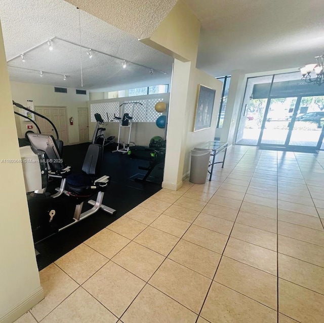workout area featuring tile patterned floors, a textured ceiling, track lighting, baseboards, and a chandelier