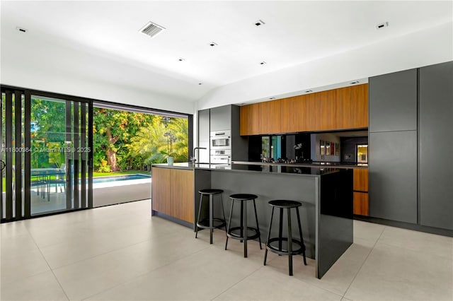 4275 Prairie Ave, Miami Beach, FL 33140 - kitchen with modern cabinets, a kitchen bar, brown cabinetry, vaulted ceiling, and dark countertops