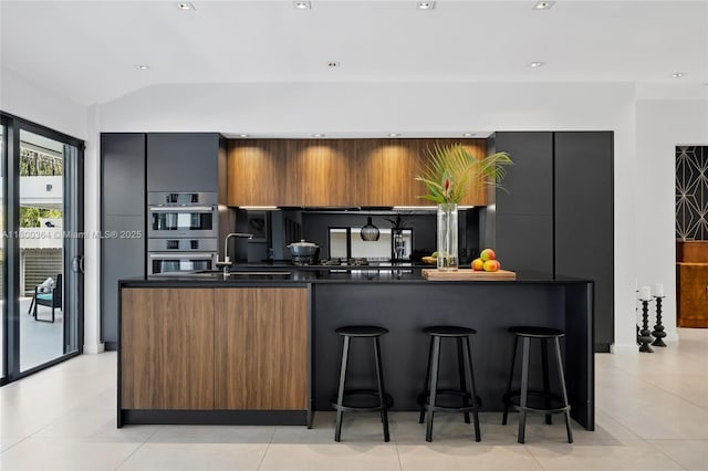 4275 Prairie Ave, Miami Beach, FL 33140 - kitchen featuring modern cabinets, dark countertops, double oven, a kitchen breakfast bar, and vaulted ceiling