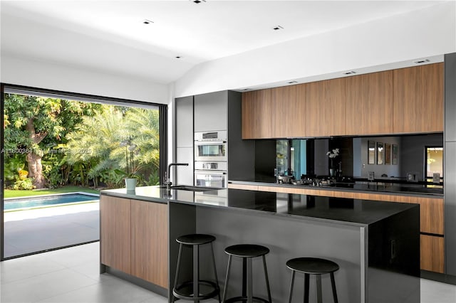 4275 Prairie Ave, Miami Beach, FL 33140 - kitchen featuring modern cabinets, brown cabinetry, vaulted ceiling, a kitchen bar, and dark countertops