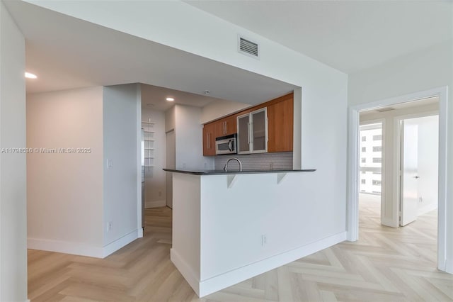 335 S Biscayne Blvd Unit 1012, Miami, FL 33131 - kitchen featuring stainless steel microwave, brown cabinets, dark countertops, a kitchen bar, and baseboards