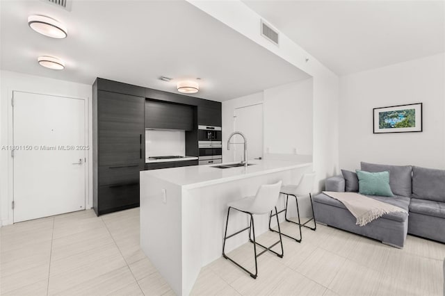 kitchen with a kitchen bar, a sink, a peninsula, light countertops, and dark cabinetry