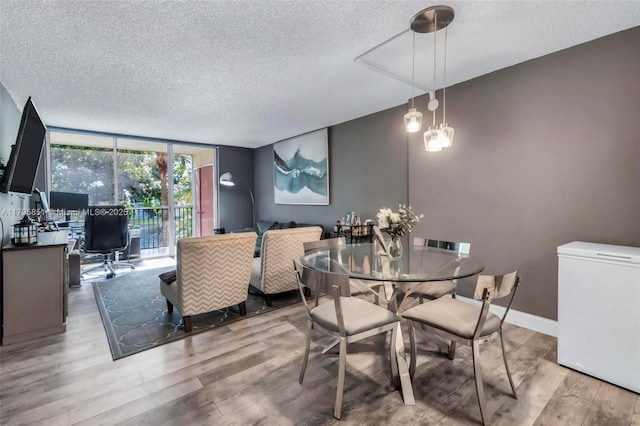 dining space featuring a textured ceiling, wood finished floors, a wall of windows, an office area, and baseboards