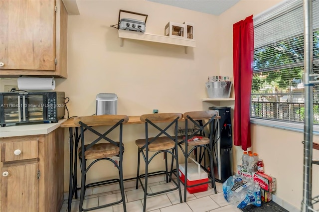 kitchen with light tile patterned flooring, a breakfast bar area, baseboards, and light countertops