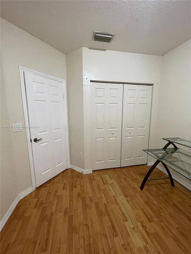 unfurnished bedroom with light wood-type flooring, baseboards, a closet, and a textured ceiling