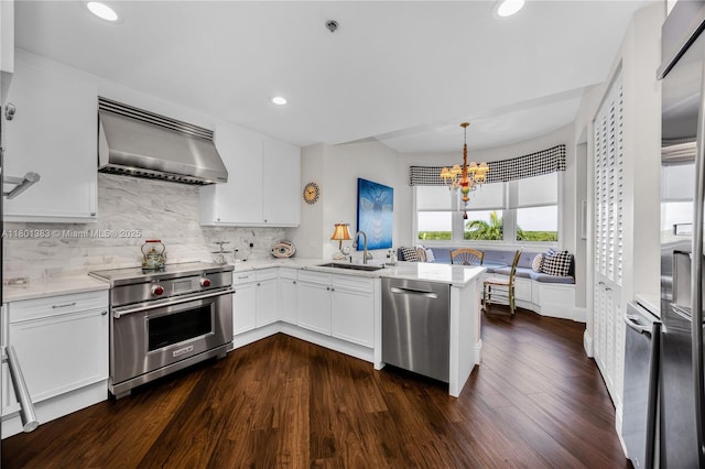 kitchen featuring stainless steel appliances, wall chimney exhaust hood, a sink, recessed lighting, and tasteful backsplash