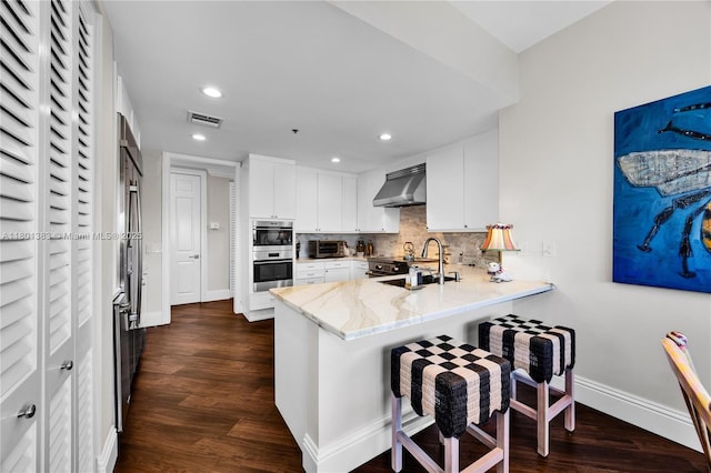 kitchen with a peninsula, ventilation hood, stainless steel double oven, baseboards, and a sink