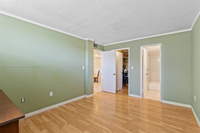unfurnished bedroom featuring light wood-style flooring, a textured ceiling, a walk in closet, ornamental molding, and baseboards
