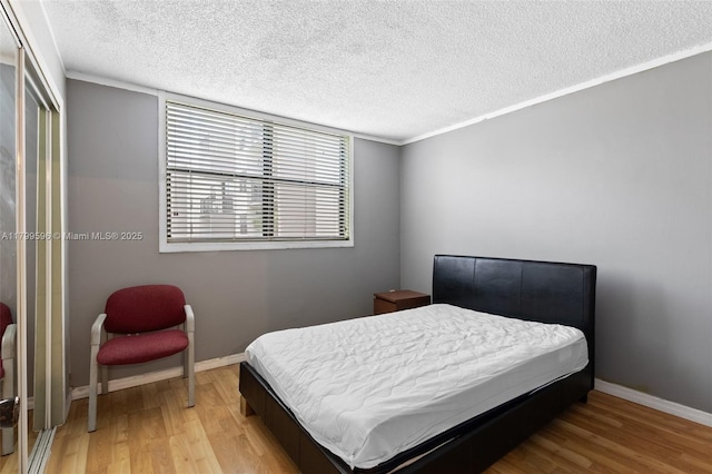bedroom featuring light wood-type flooring, a textured ceiling, and baseboards