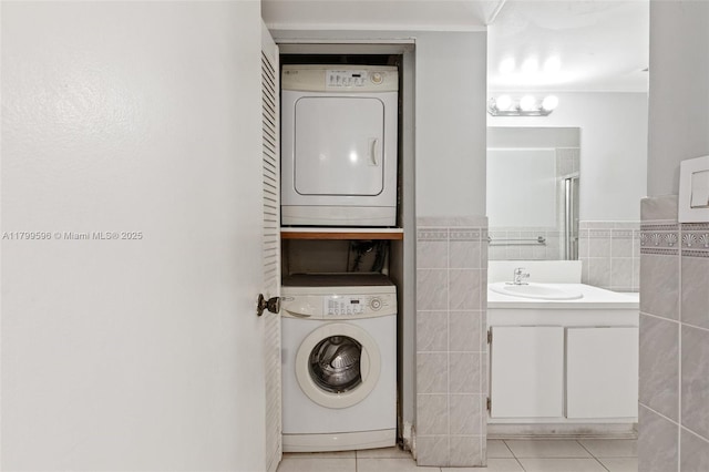 washroom featuring estacked washer and dryer, light tile patterned floors, tile walls, and a wainscoted wall