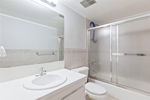 bathroom with tile walls, toilet, vanity, and combined bath / shower with glass door