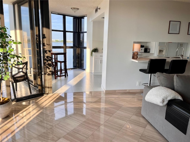 4000 NE Towwerside Ter Unit 1101, Miami, FL 33138 - living area featuring a wall of windows, a water view, a textured ceiling, light tile patterned floors, and baseboards