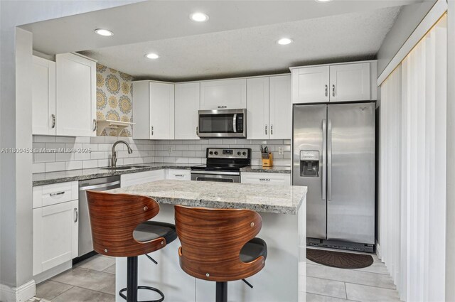 2323 NW 37th Ave, Coconut Creek, FL 33066 - kitchen with stainless steel appliances, white cabinets, a breakfast bar area, a kitchen island, and light stone countertops