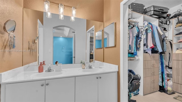 bathroom with a textured wall, a spacious closet, and double vanity