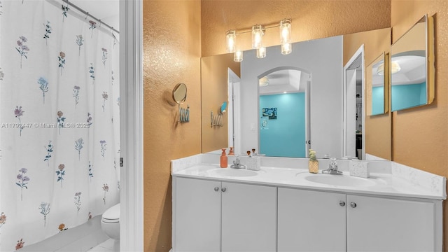 bathroom with toilet, double vanity, and a textured wall