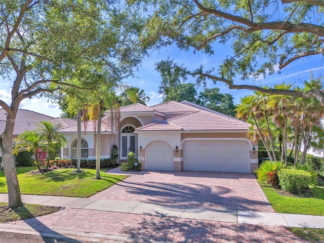 2623 Oakbrook Dr, Weston, FL 33332 - mediterranean / spanish-style home with an attached garage, decorative driveway, stucco siding, a front lawn, and a tiled roof