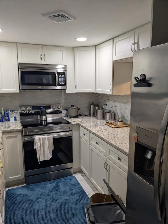 kitchen featuring stainless steel appliances, backsplash, white cabinets, and light stone counters