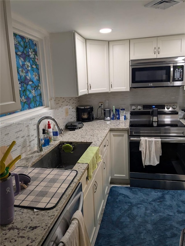 kitchen featuring appliances with stainless steel finishes, tasteful backsplash, white cabinetry, a sink, and light stone countertops
