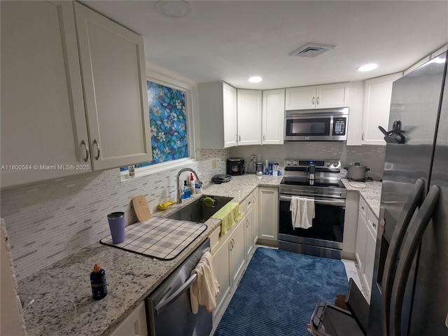 kitchen with appliances with stainless steel finishes, a sink, decorative backsplash, white cabinets, and light stone counters