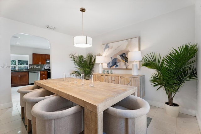 dining room featuring baseboards, arched walkways, and light tile patterned floors