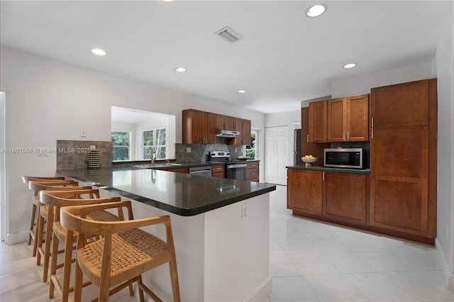 kitchen with stainless steel appliances, a peninsula, dark countertops, backsplash, and under cabinet range hood
