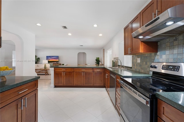 kitchen featuring stainless steel appliances, under cabinet range hood, a sink, a peninsula, and decorative backsplash