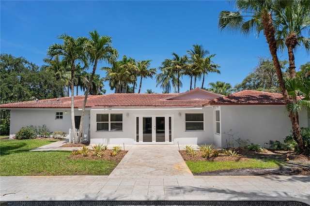 view of front facade featuring french doors, a tile roof, a front lawn, and stucco siding