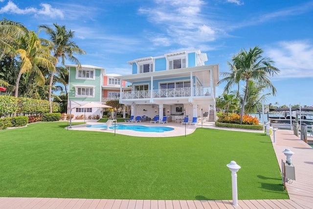 rear view of house with a balcony, a patio area, a lawn, and an outdoor pool