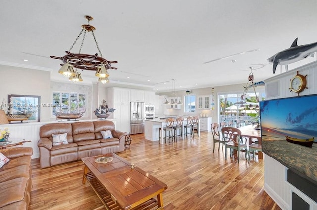 living area with light wood-style floors, recessed lighting, healthy amount of natural light, crown molding, and a chandelier
