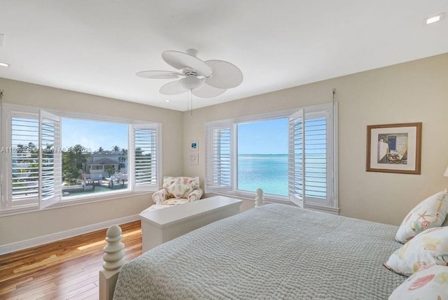 bedroom with wood finished floors, a ceiling fan, baseboards, and a water view