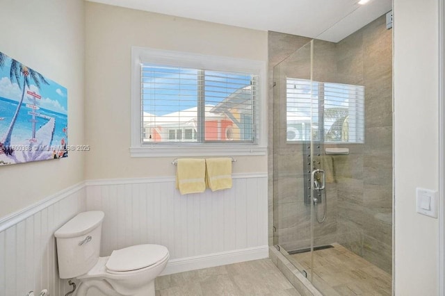 full bath featuring healthy amount of natural light, a wainscoted wall, toilet, and a stall shower