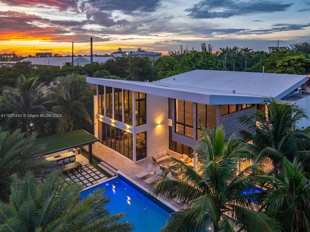 521 Holiday Dr, Hallandale Beach, FL 33009 - back of property at dusk featuring an outdoor pool and a patio area