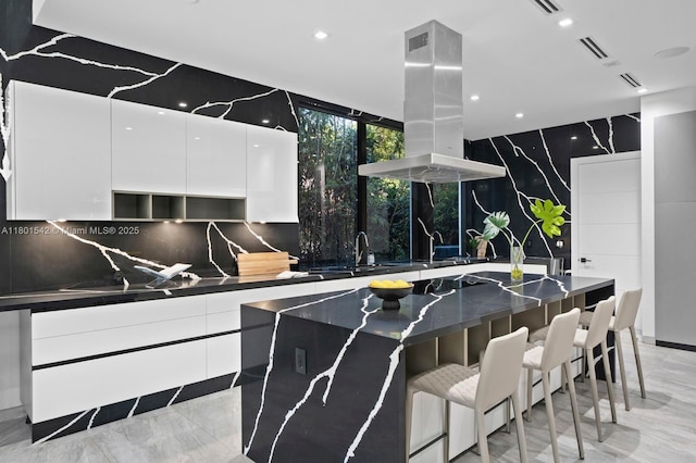 521 Holiday Dr, Hallandale Beach, FL 33009 - kitchen with modern cabinets, island exhaust hood, dark countertops, white cabinets, and a kitchen bar