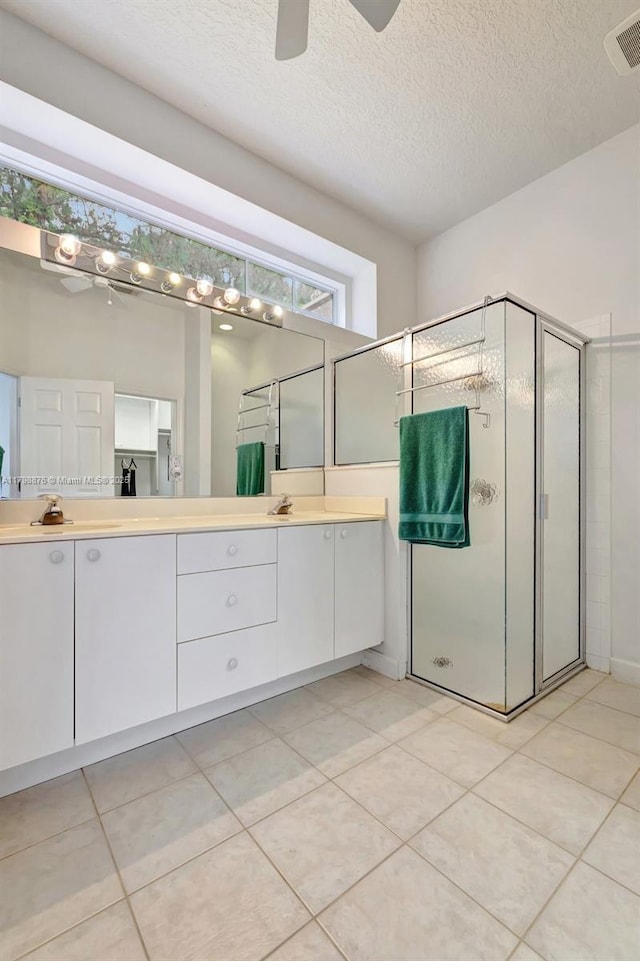 full bath with a stall shower, double vanity, a textured ceiling, a ceiling fan, and tile patterned flooring