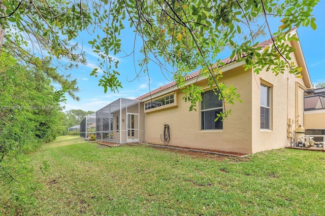 back of property with stucco siding, a lawn, and a lanai
