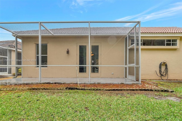back of house featuring stucco siding, glass enclosure, a patio, and a yard